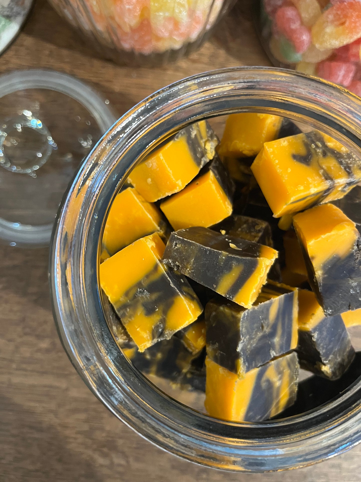 An open jar of chunky cut cubes of fudge coloured bright orange marbled with dark brown. 