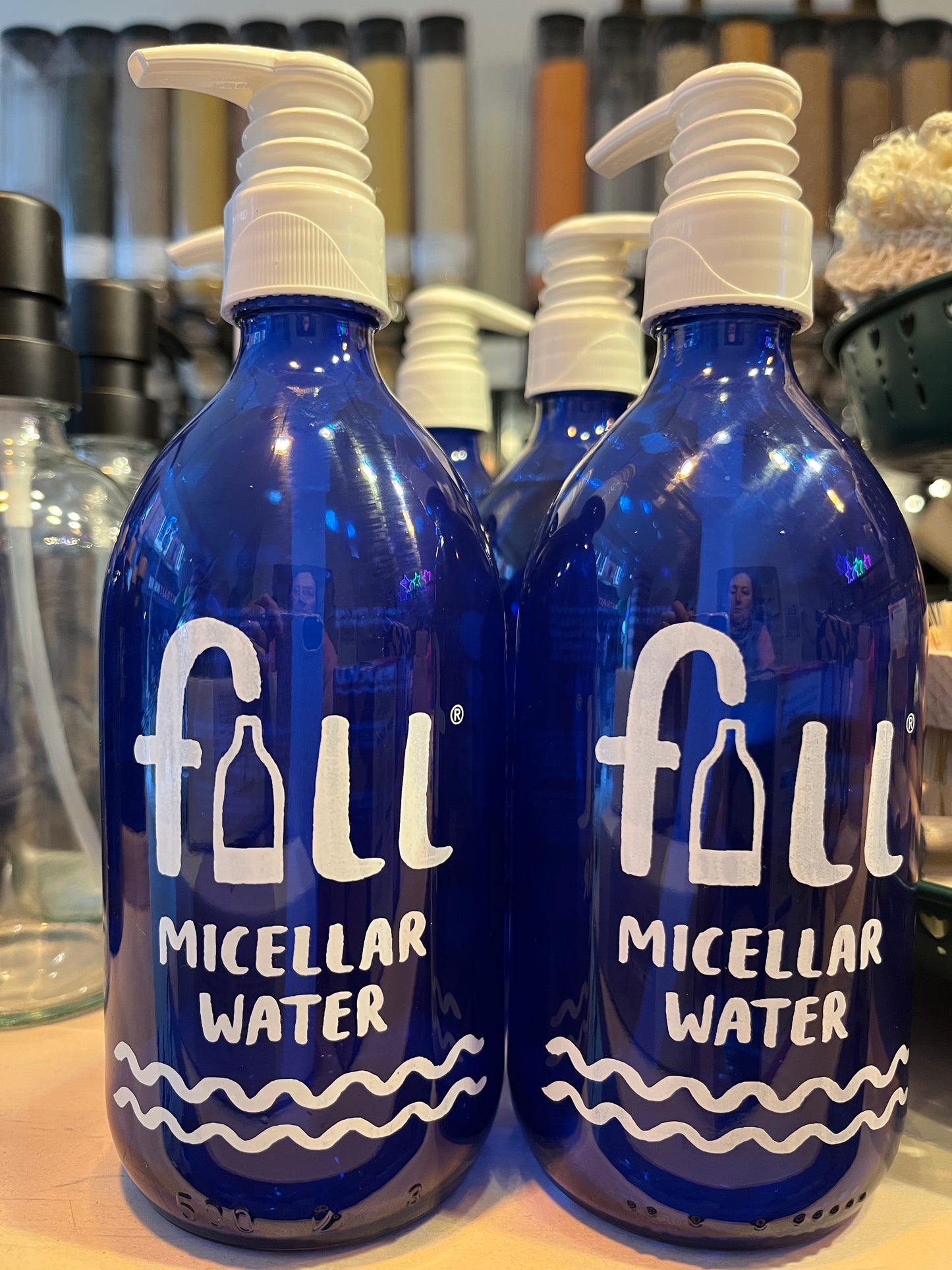 Blue glass bottles with white pumps screen printed in white with the words 'fill MICELLAR WATER' and two wavy lines.