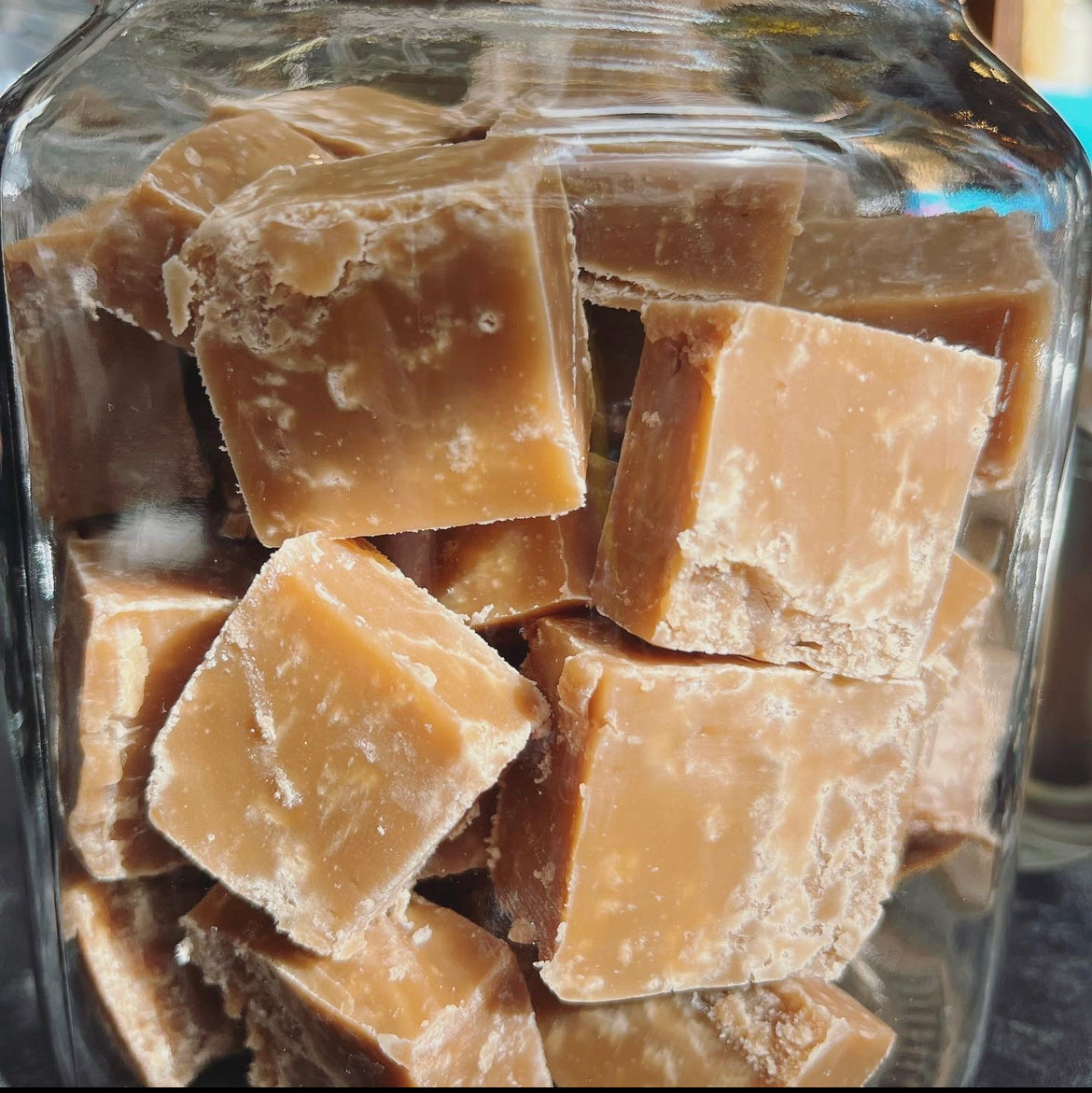 Golden brown crumbly blocks of vegan fudge piled high in a glass jar.