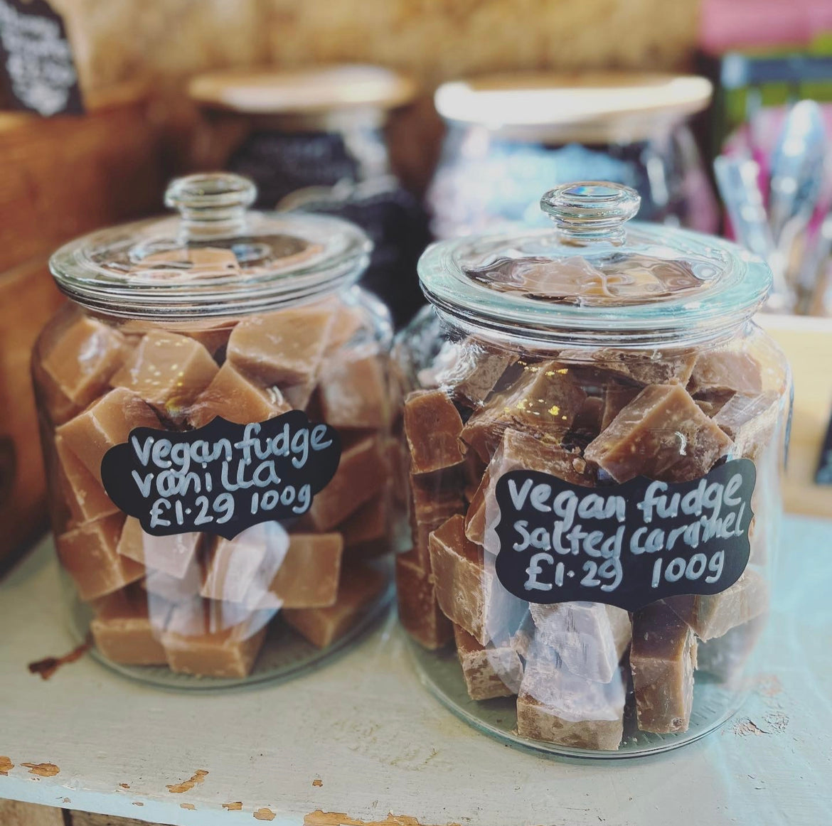 Two glass sweet shop jars holding vanilla and salted caramel fudge with handwritten blackboard labels.